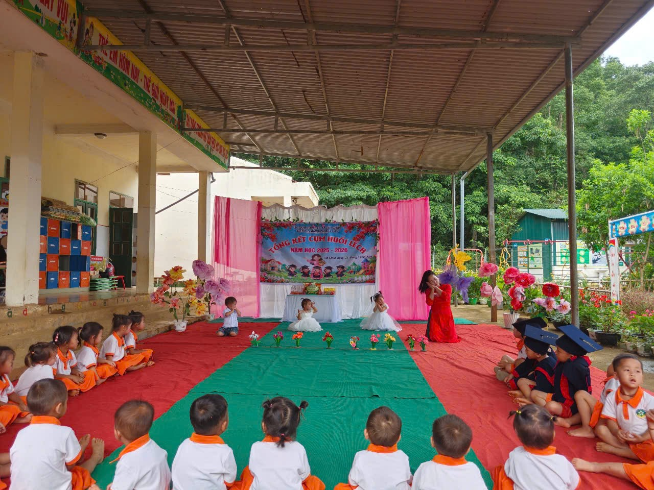'A group of children sitting on a red and green carpet

Description automatically generated'